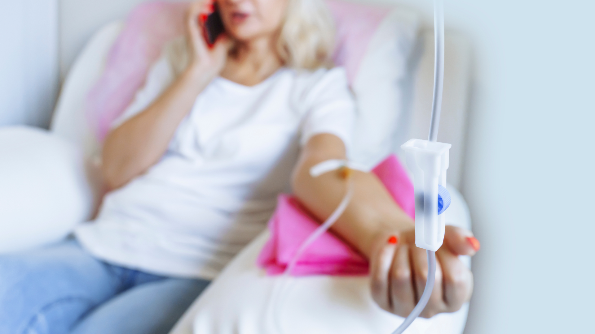Woman reclining on a sofa receiving an IV drip while on her phone, IV line in focus
